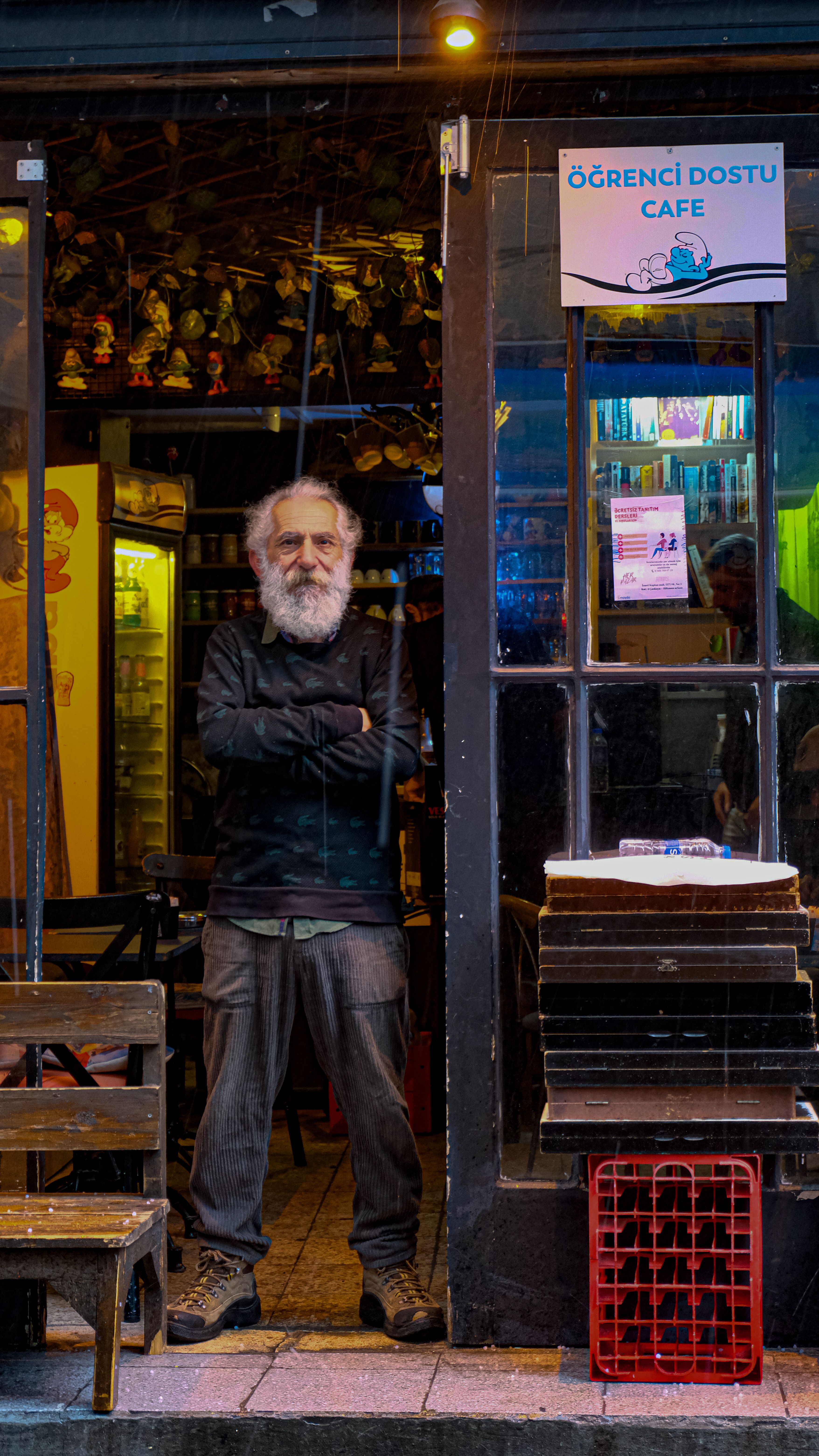 A bearded man standing at the entrance of a cozy, eclectic cafe with unique decor.