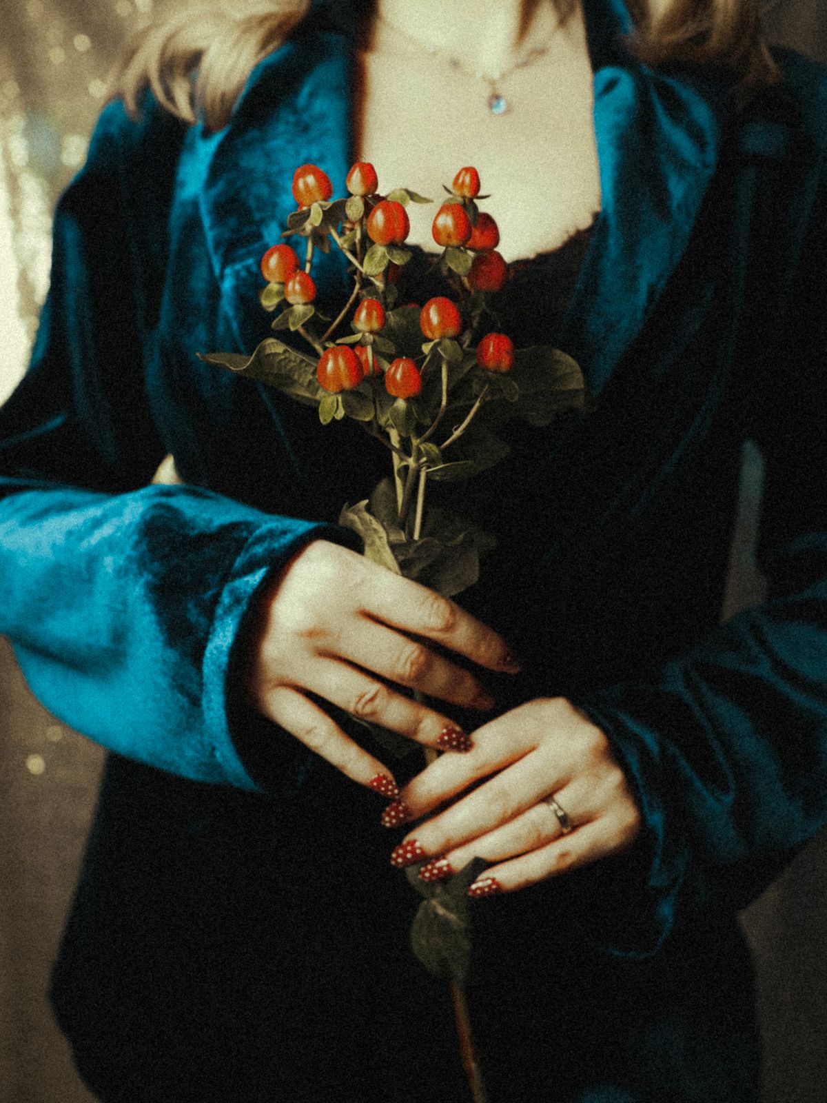 Elegant woman in blue velvet jacket holding vibrant red berries against a textured backdrop.