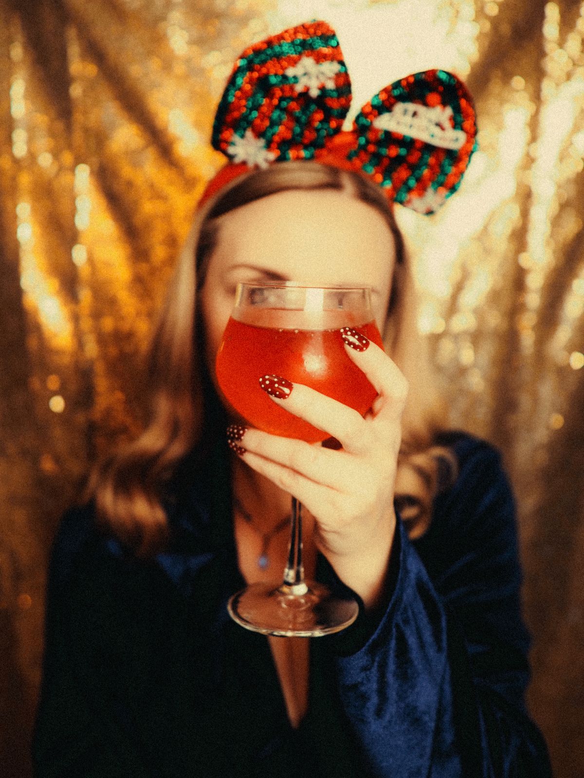 A woman in velvet holds a cocktail with a festive bow headband.