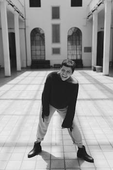 黑白时尚照片中，一个人在城市环境中穿着时尚服装大笑