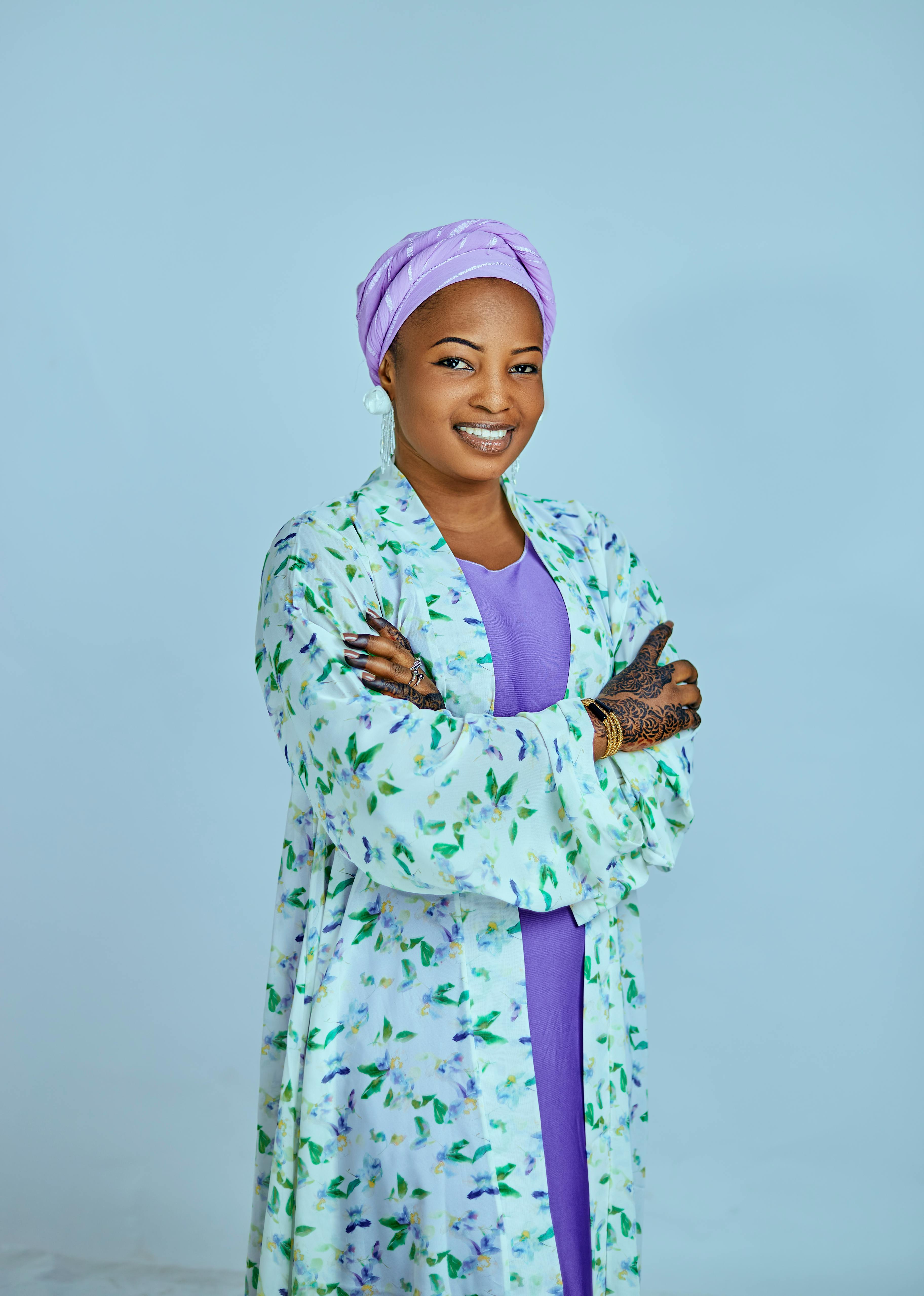 Portrait of a woman in traditional attire with crossed arms against a blue background.