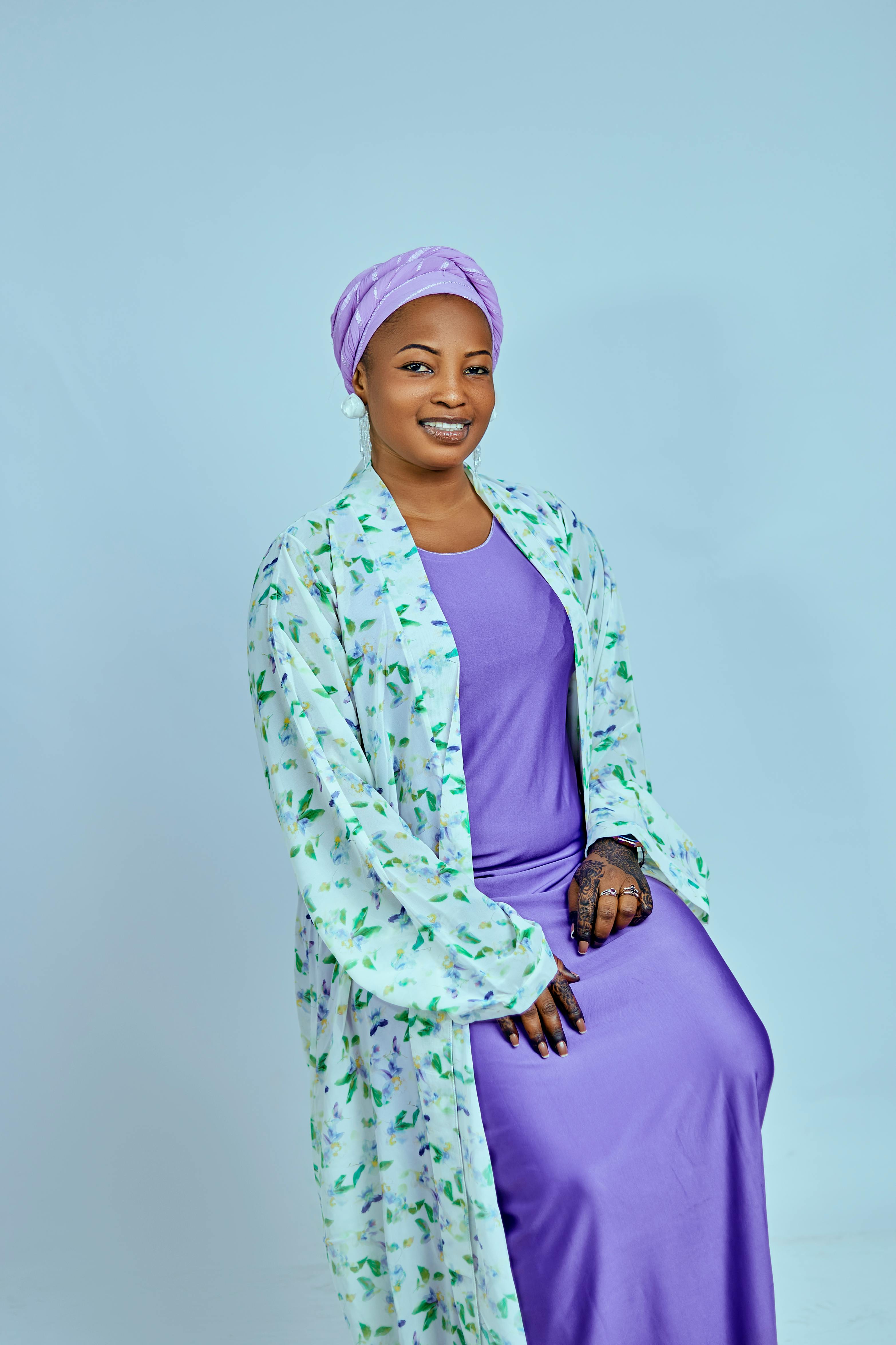 A graceful woman dressed in purple sitting against a light blue background.