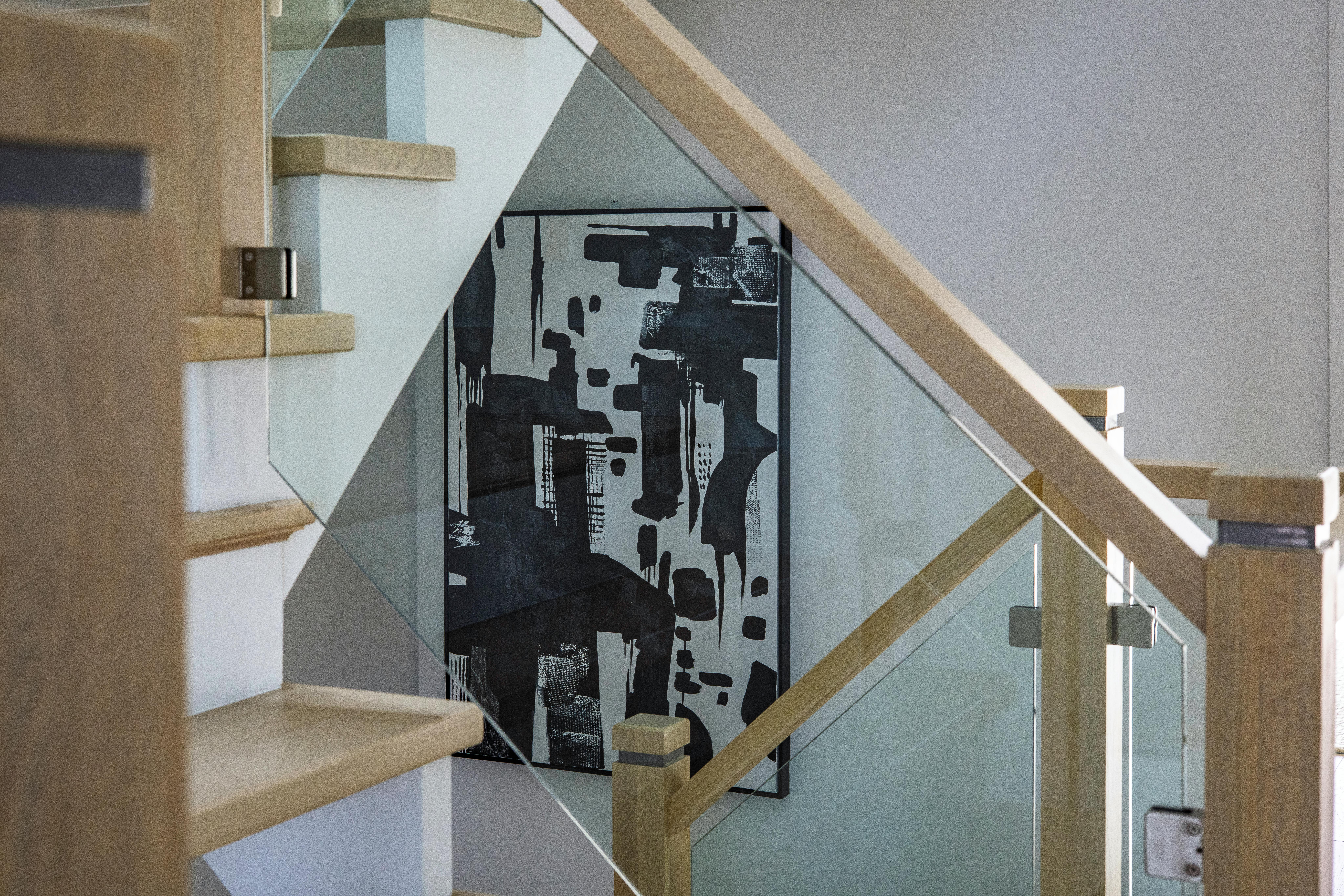 Gratuit Un escalier moderne avec des marches en bois et une rampe en verre mettant en valeur une œuvre d'art murale abstraite. Photos
