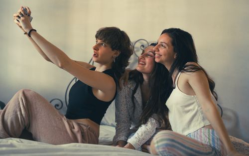 Free Three young women taking a selfie on a bed, enjoying a relaxing indoor moment. Stock Photo