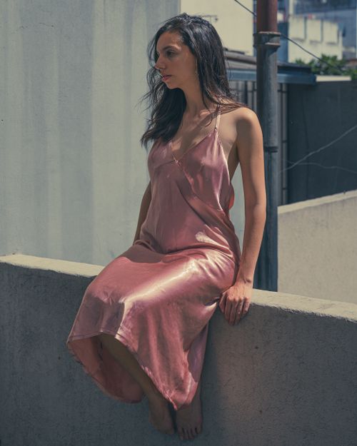 Free Woman in a silky pink dress sitting on a concrete ledge under the sun. Stock Photo