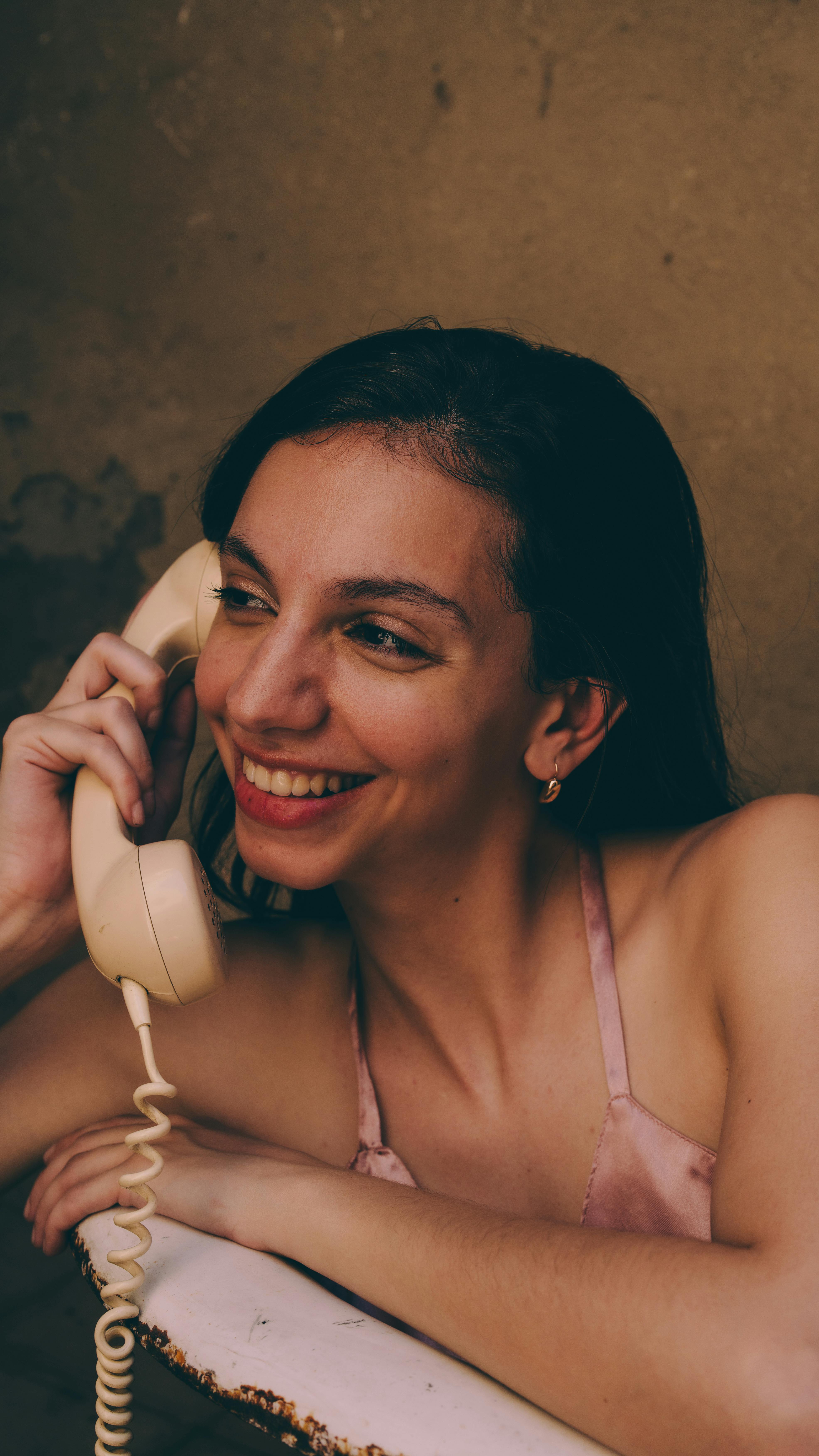 Gratis Smilende kvinne i rosa topp bruker en vintagetelefon innendørs. Arkivbilde