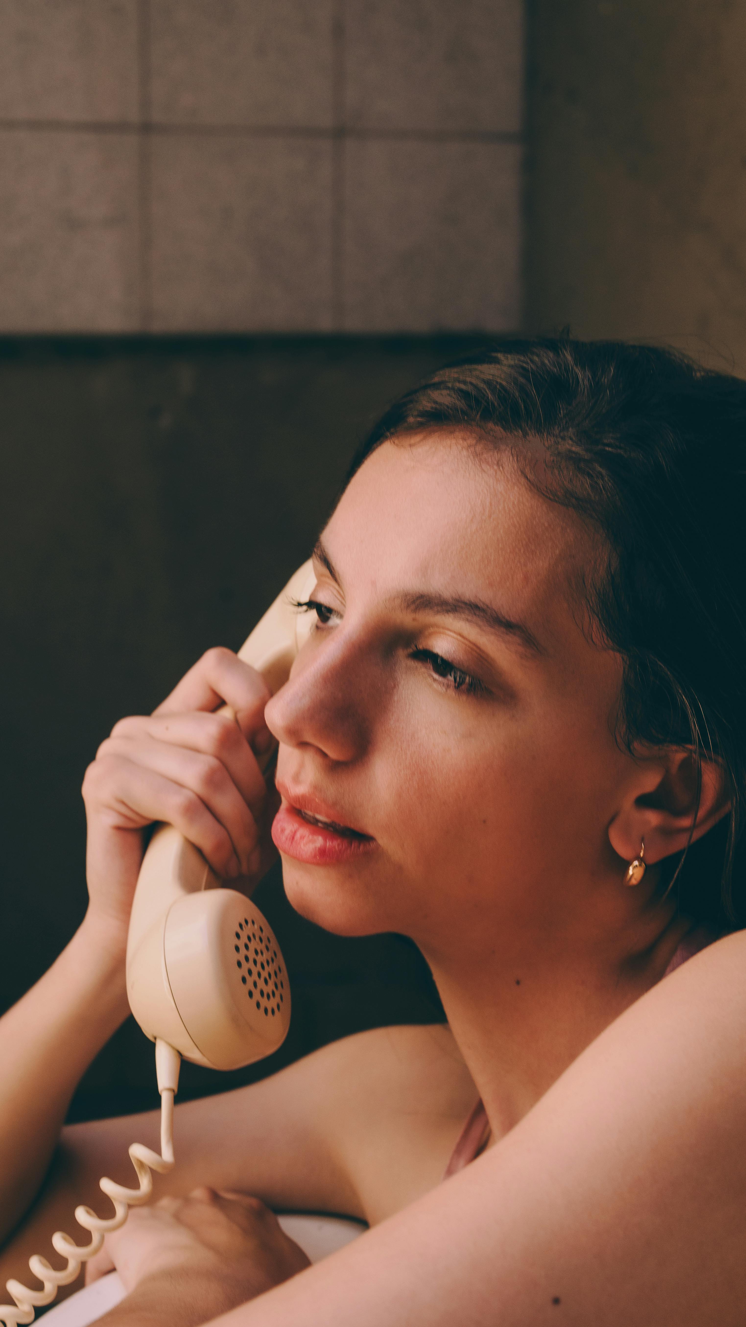 Gratis Una giovane donna usa pensierosa un telefono a disco d'epoca in casa. Foto a disposizione