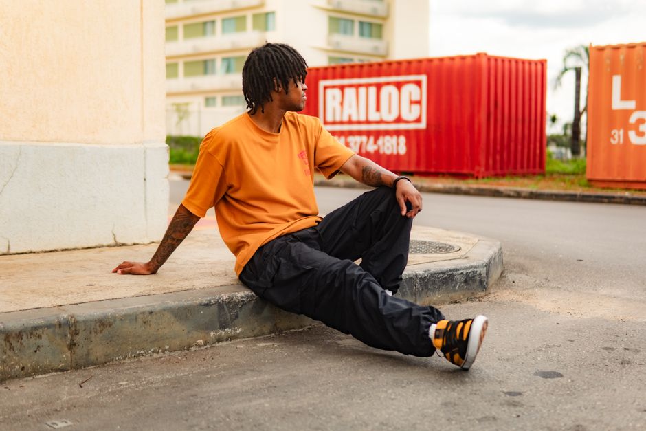 Young man in casual urban clothing sits relaxed by containers in Sete Lagoas.