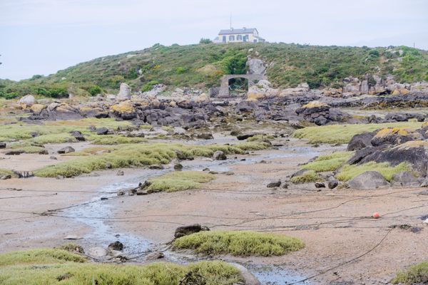 Low tide flats below a stone house and arch in Chausey