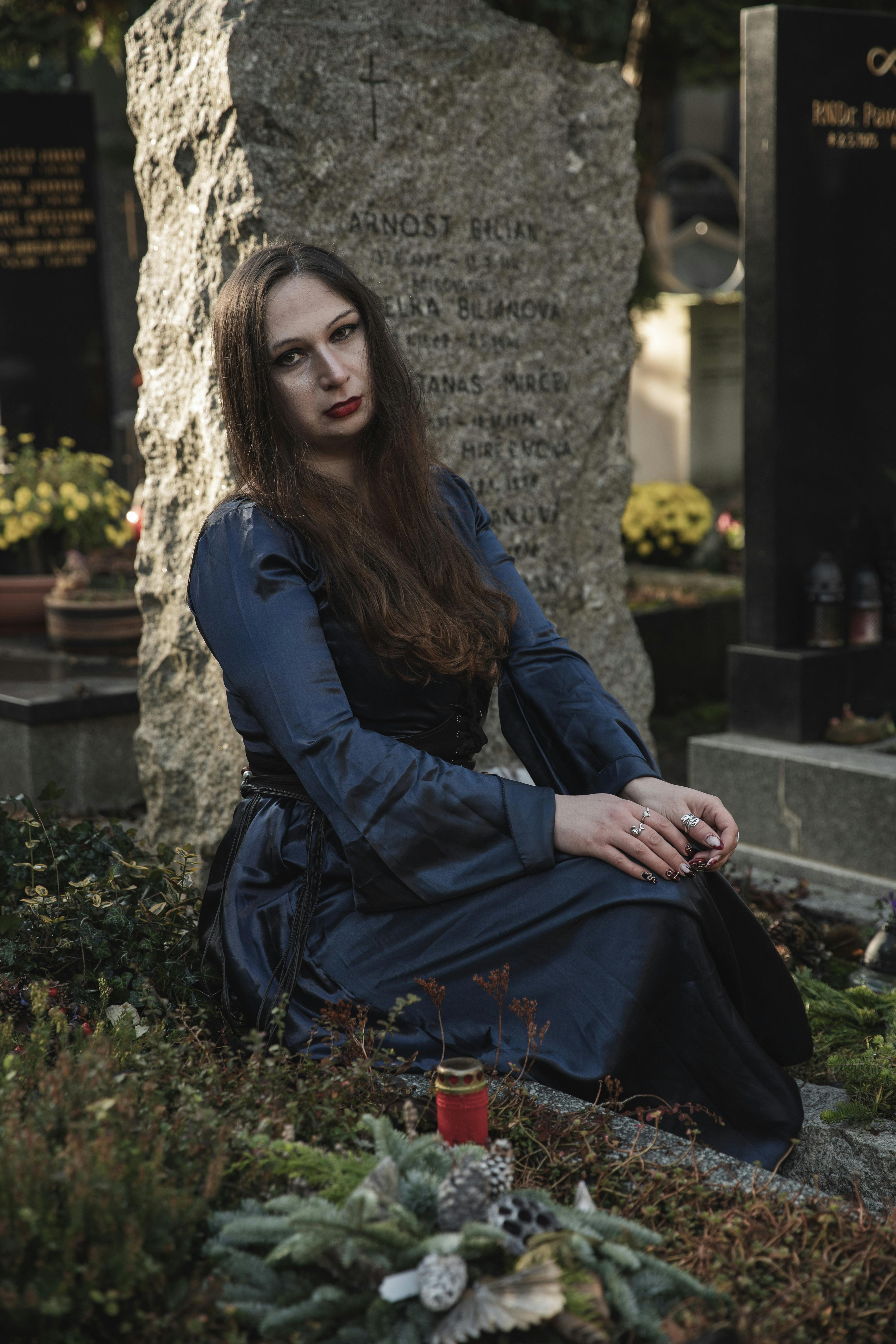 Woman in a blue dress sitting by a gravestone. Gothic atmosphere.
