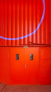 A striking red metal door with blue geometric accents, showcasing modern industrial design.