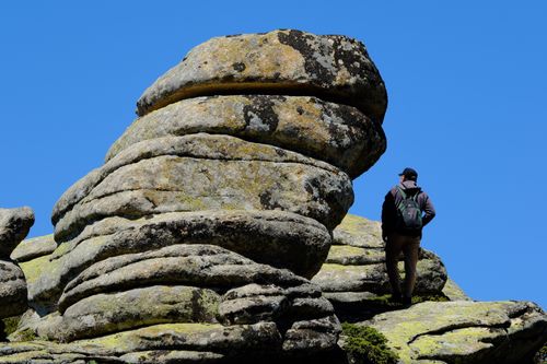 Free A hiker with a backpack observes a unique, layered rock formation under a clear blue sky. Stock Photo