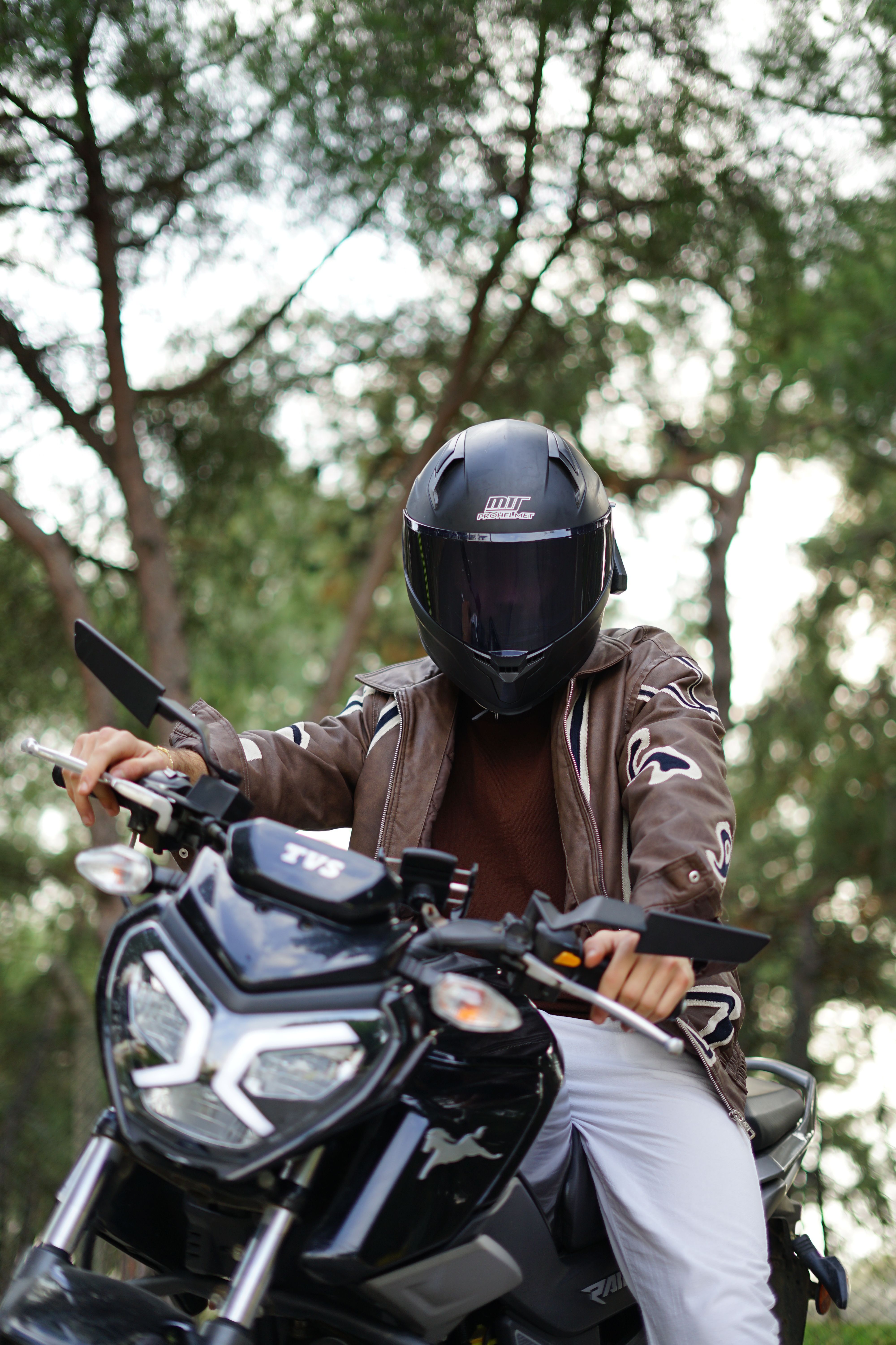 Motorcyclist wearing a helmet on a black motorcycle in a forest area, showcasing adventure and freedom.