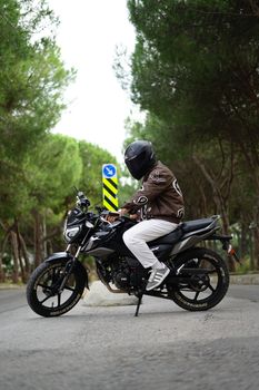 Side profile of a motorcyclist on a black bike riding through a lush green forest.