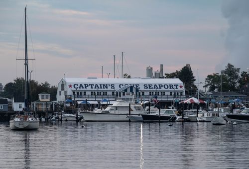 Free Serene view of Captain's Cove Seaport at sunset with various boats docked, reflecting on calm waters. Stock Photo