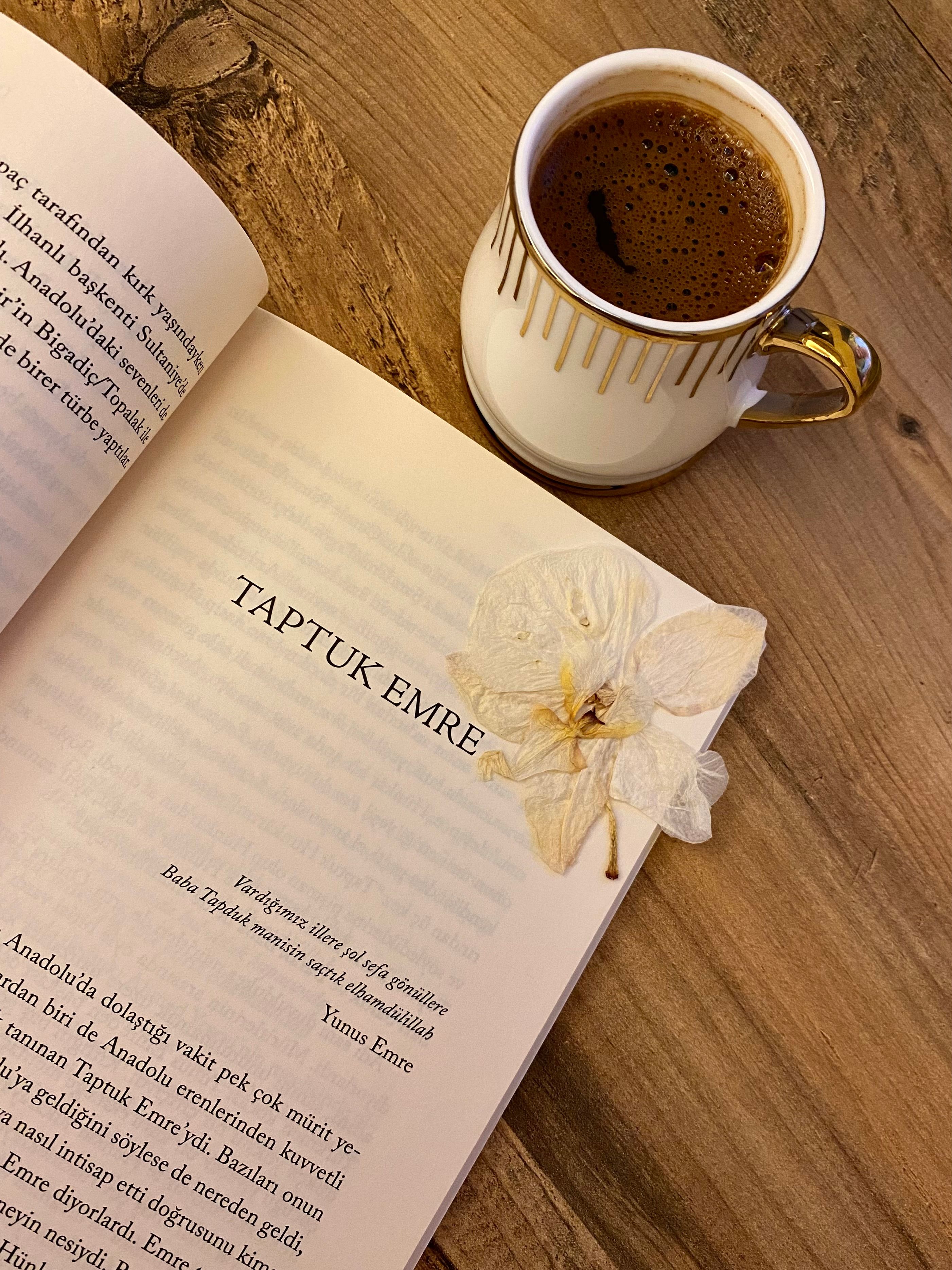 Open book with coffee and flower arrangement on wooden table.