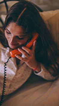 A woman talking on an orange vintage phone while relaxing indoors. Cozy atmosphere.