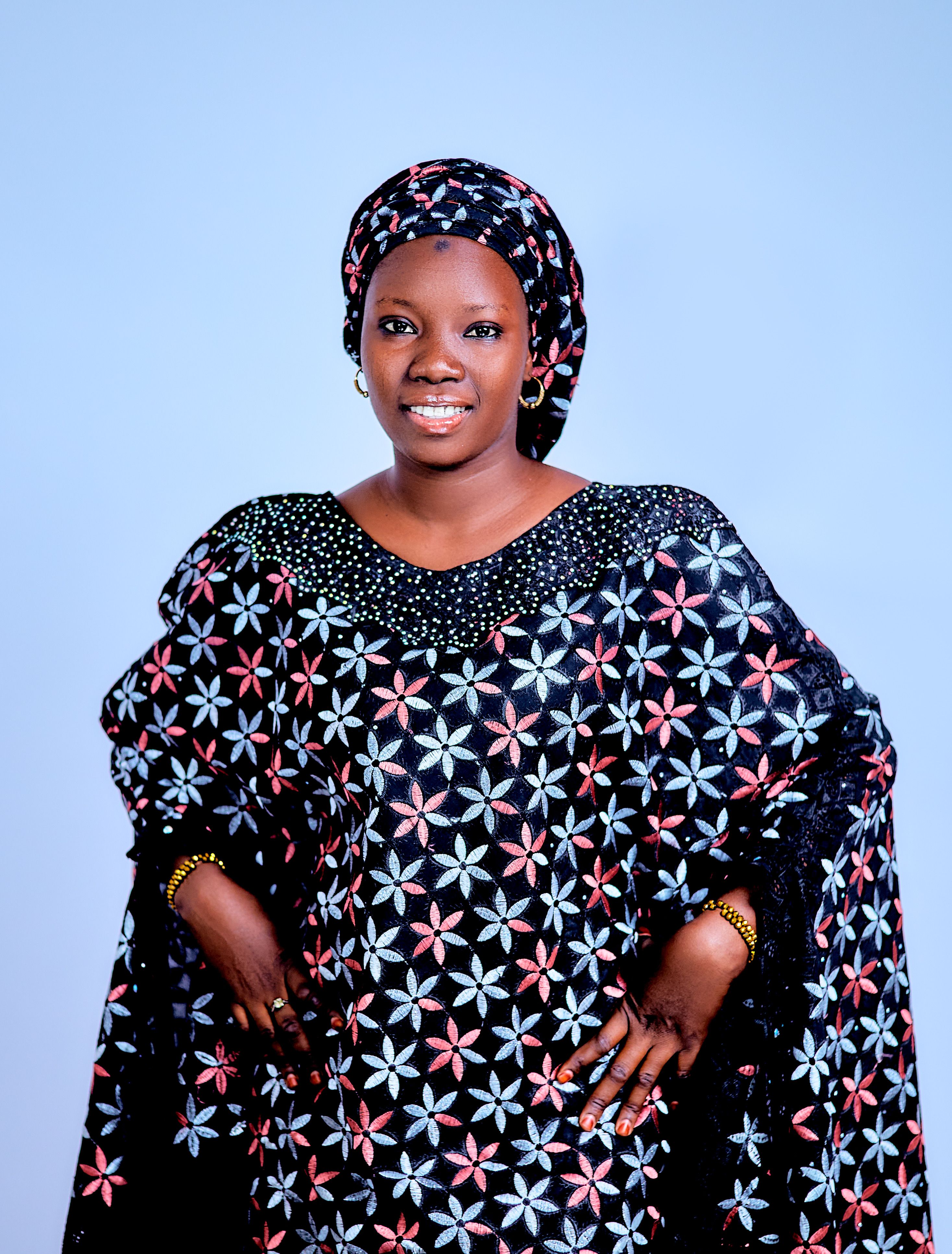 Smiling African woman in vibrant traditional attire with floral patterns.