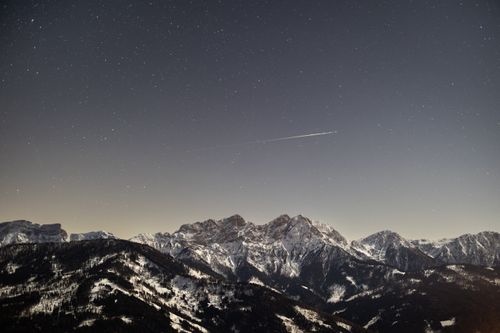 Free A serene night sky over the snow-covered Dolomites with visible stars and a distant airplane trail. Stock Photo