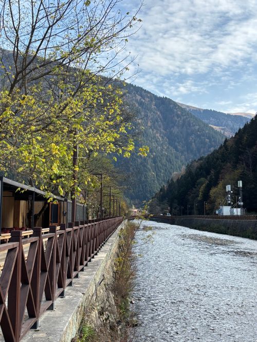 Free A tranquil river flows through a lush valley surrounded by mountains and a pathway. Stock Photo