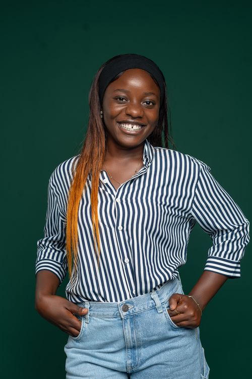 Free Confident woman smiling in a striped shirt and denim, on a green backdrop. Stock Photo