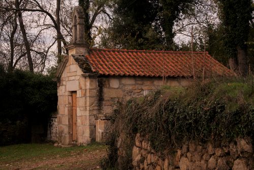 Free A small rustic stone chapel with a red-tiled roof nestled in lush greenery, providing a serene woodland retreat. Stock Photo