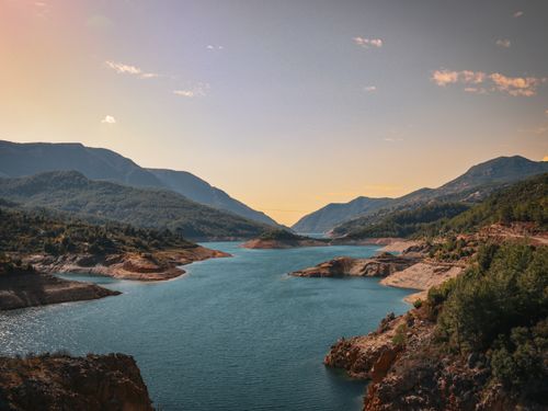 Free Breathtaking view of a serene mountain lake surrounded by lush forests at sunset. Stock Photo