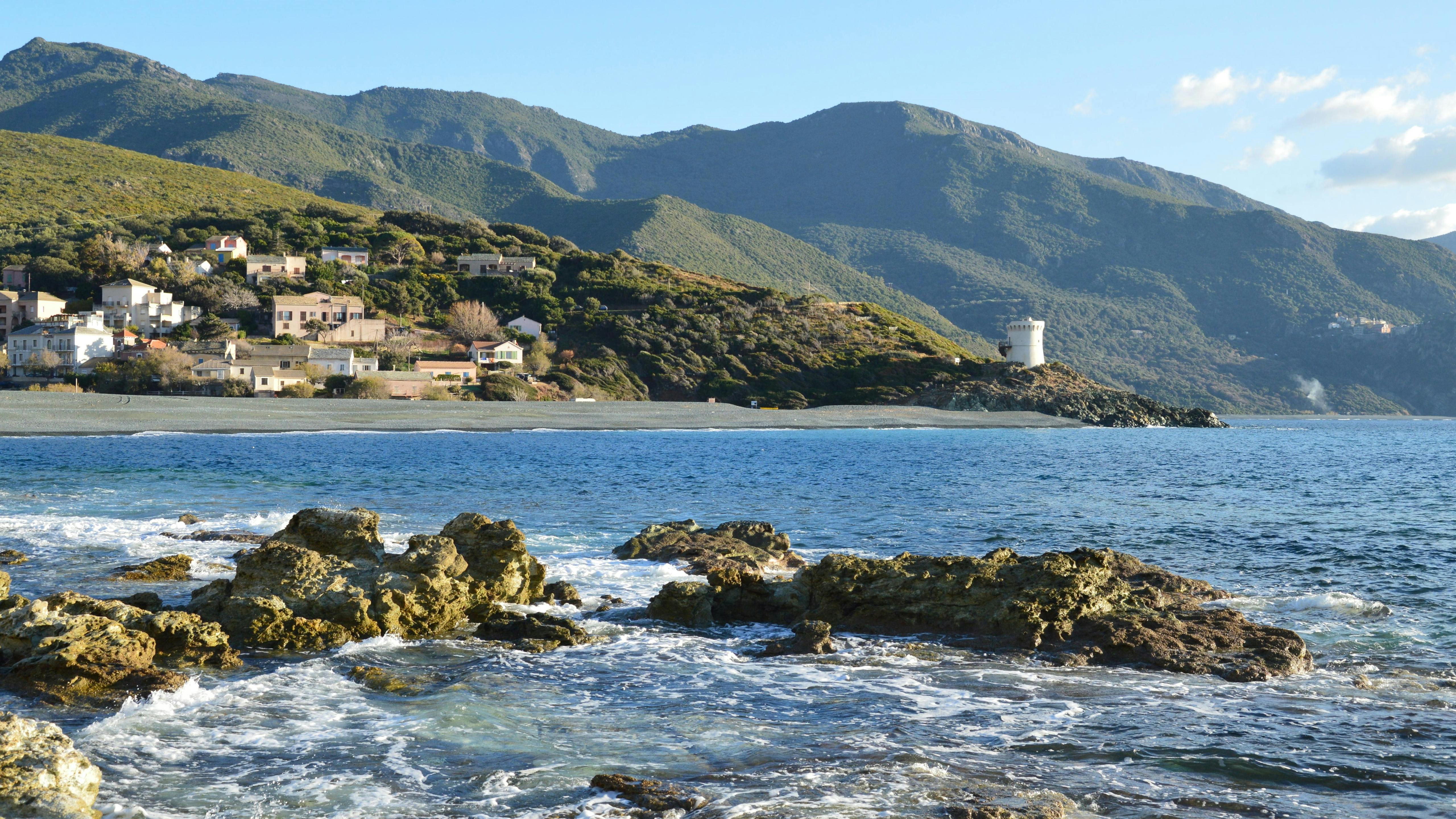 Beautiful coastal landscape in Ogliastro, Corse, France with rocky shoreline and distant mountains.