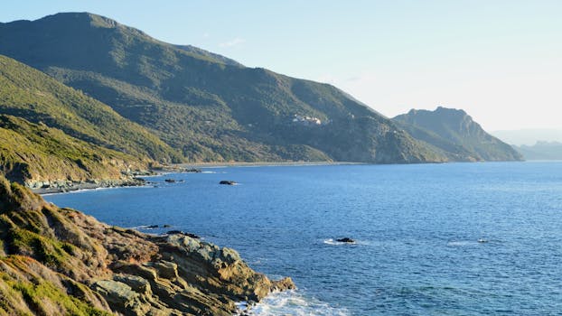 Breathtaking view of Ogliastro's rugged coastline in Corsica with lush hills and vibrant blue sea.