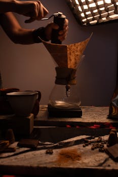 Close-up of hand grinding coffee beans and using Chemex in low light.