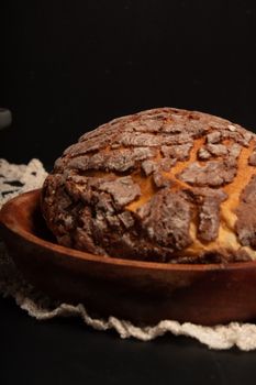 A beautifully baked concha bread sits in a rustic wooden bowl against a black background.