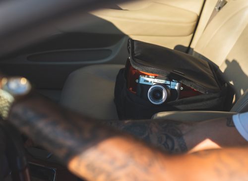Free A man with tattoos drives a car with a camera on the front seat. Stock Photo