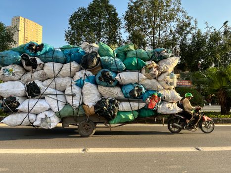 Motorbike overloaded with colorful cargo bags on a sunny street with green helmeted rider.