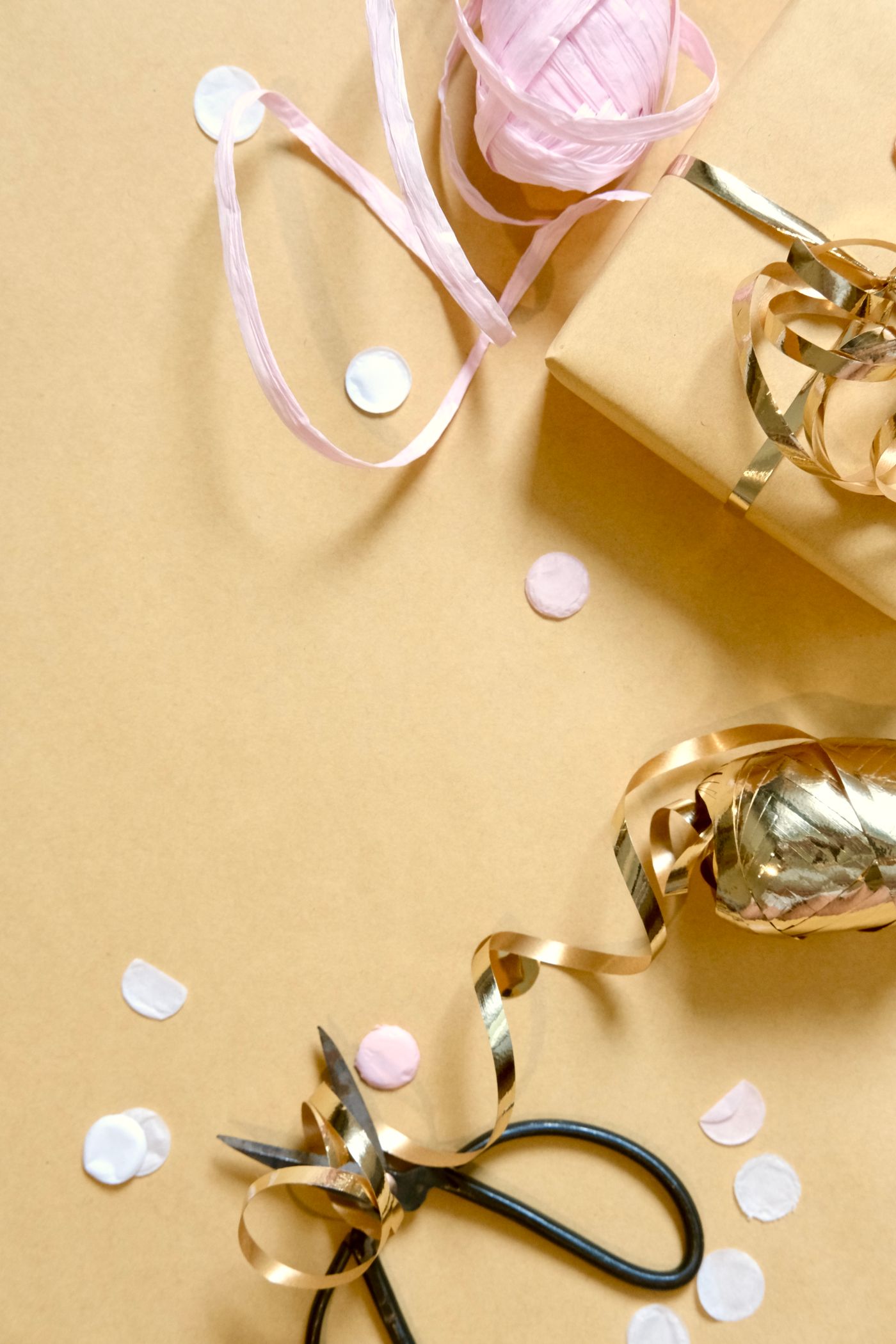 Gift wrapping materials arranged with ribbon, scissors, paper, and confetti