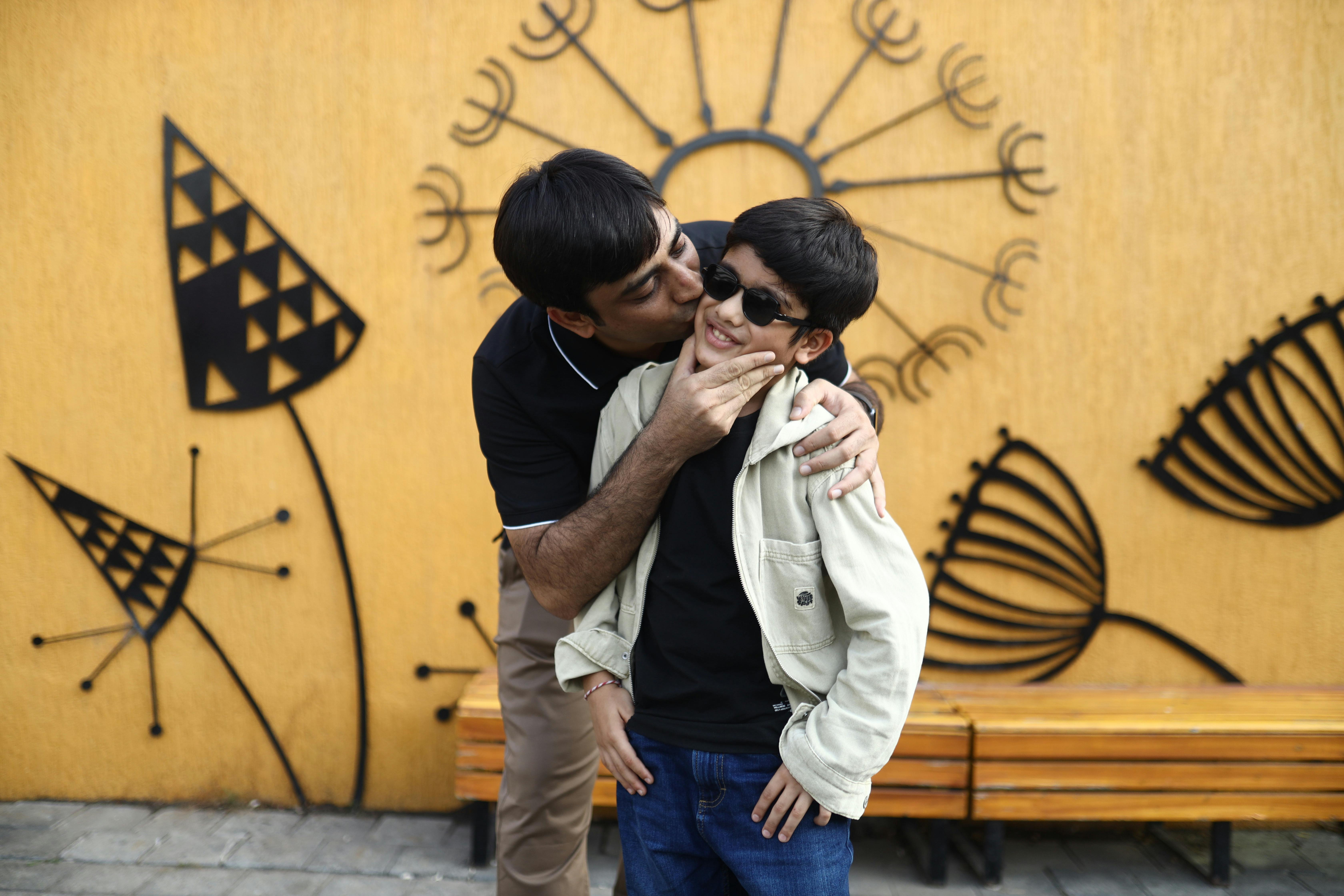 Joyful father and son sharing a playful moment outdoors against artistic wall backdrop.