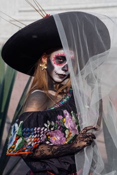 Woman with Day of the Dead makeup wearing traditional Mexican attire and hat.