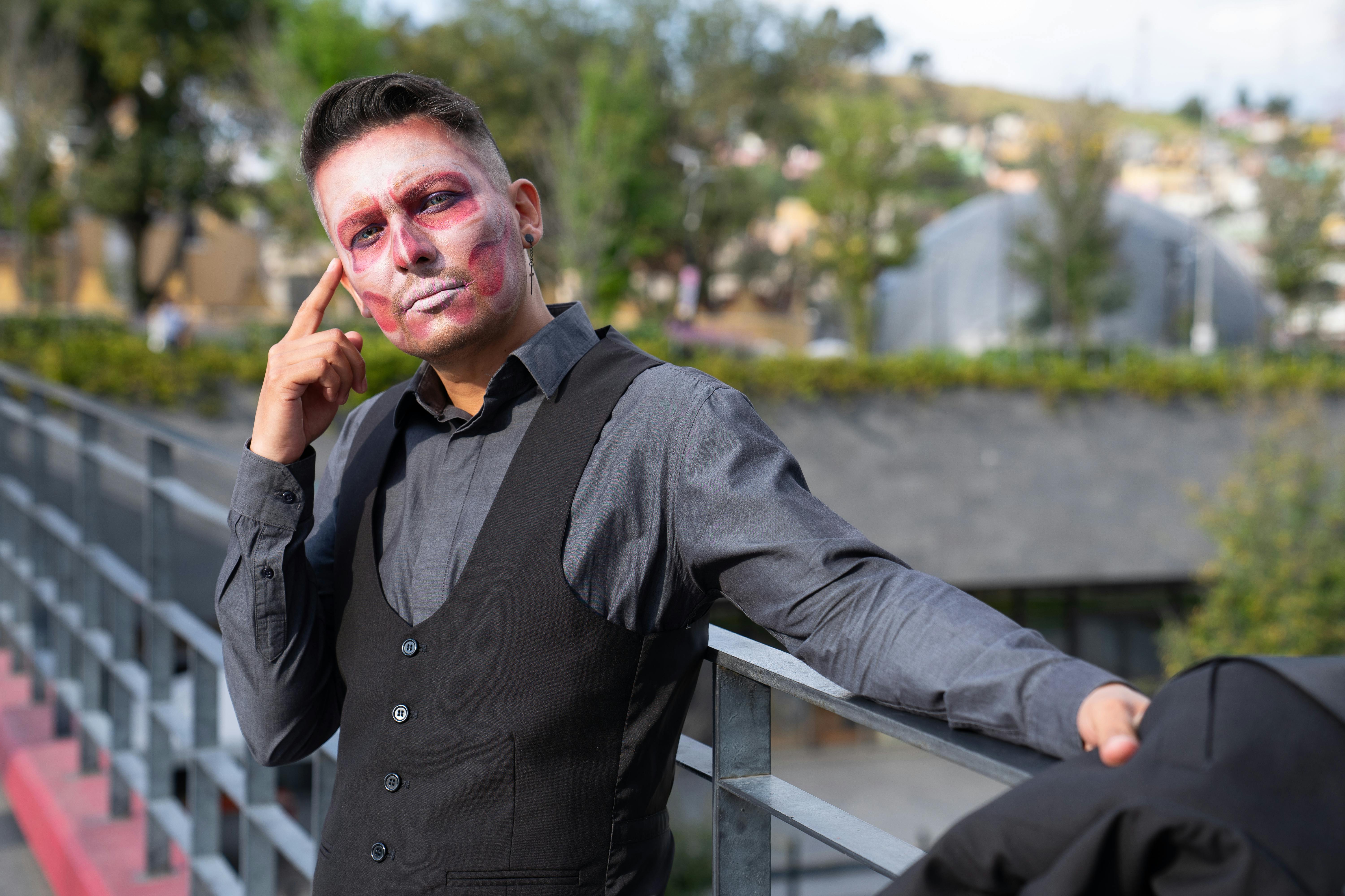 Gratis Un uomo con il viso truccato in modo artistico posa con sicurezza all'aperto, su uno sfondo sfocato. Foto a disposizione