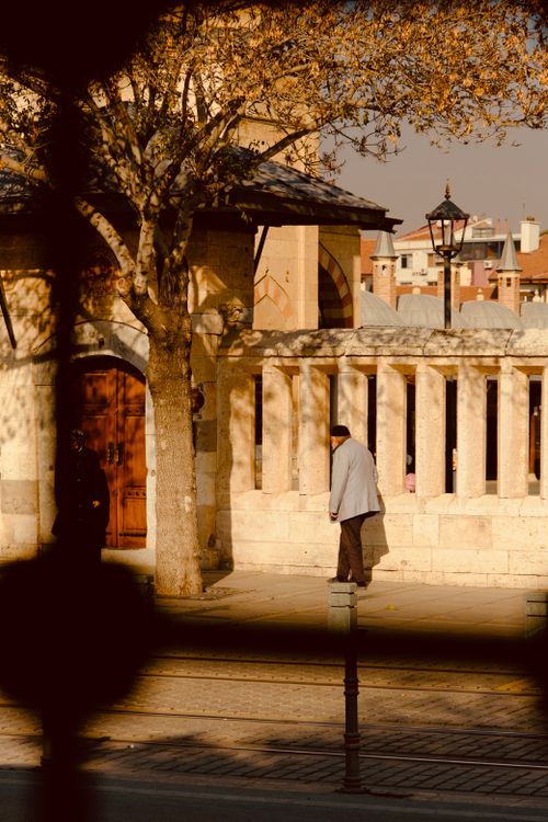 Free A solitary man walks past a historic stone building during autumn with warm lighting. Stock Photo