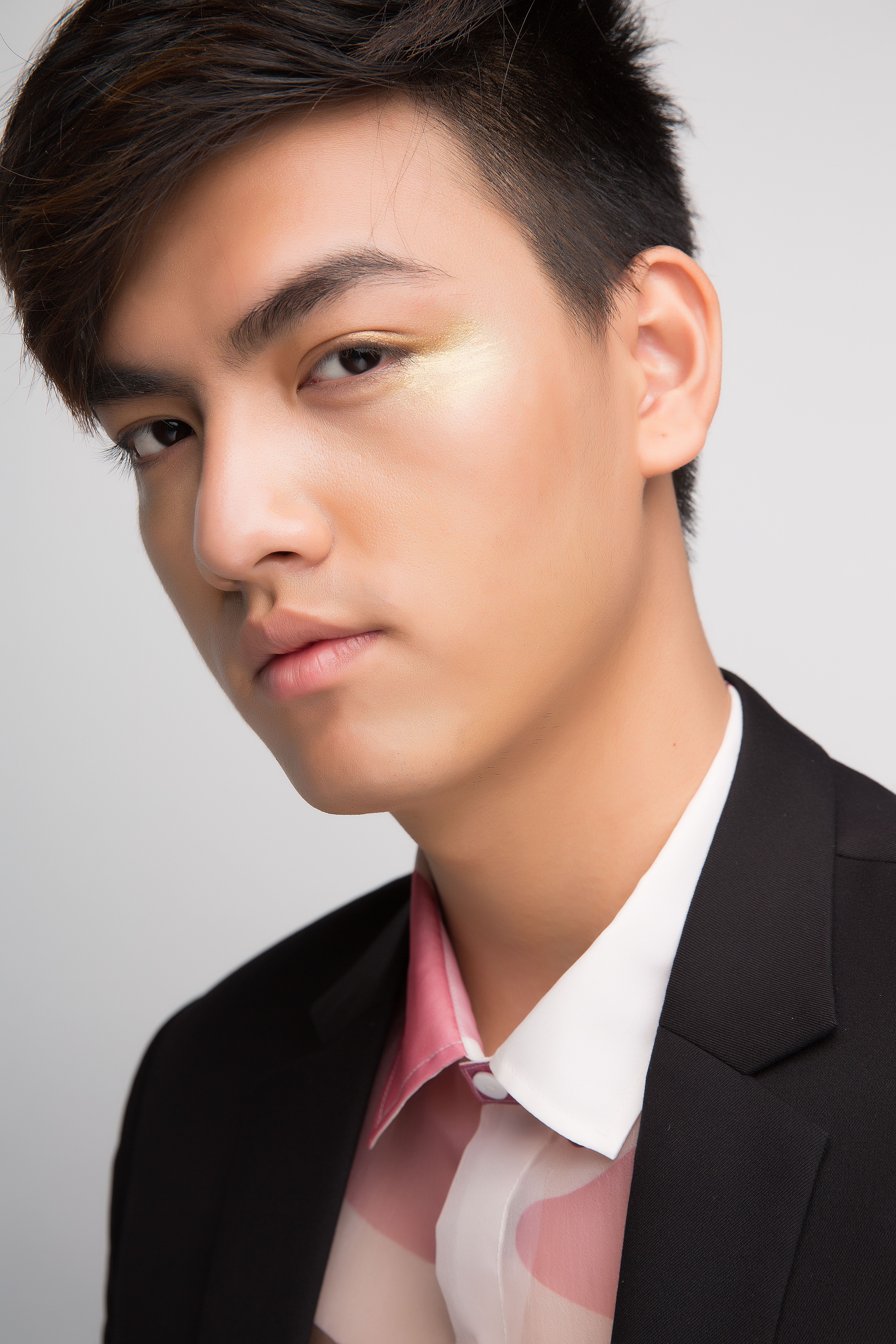 Close-up portrait of a young adult wearing a fashionable suit in a studio setting.