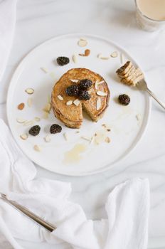 Delicious pancakes topped with blackberries and almond slices on a white plate.