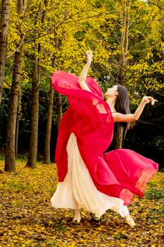 A woman dancing gracefully in a bright red dress amidst a serene autumn forest scene.