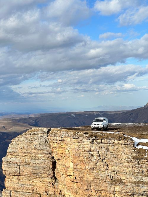 Free Adventure SUV navigating dramatic cliff edge under vast blue sky and clouds. Stock Photo