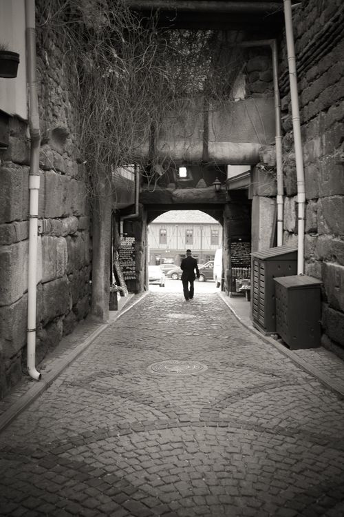 Free Dramatic black and white photo of a man walking down a historic stone alleyway. Stock Photo