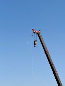 A construction crane with the moon in the background against a clear blue sky, symbolizing industry.