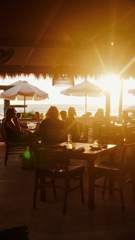 Casual diners enjoy a beachfront sunset under umbrellas, creating a warm evening ambiance.