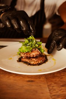 A chef skillfully garnishes a dish of grilled octopus with fresh greens on a white plate.
