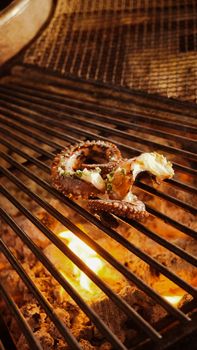 Close-up of a grilled octopus tentacle sizzling over an open flame, highlighting charred textures.