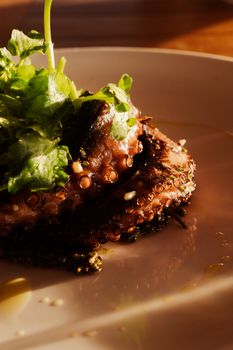 Close-up of a gourmet octopus dish garnished with fresh greens on a white plate.