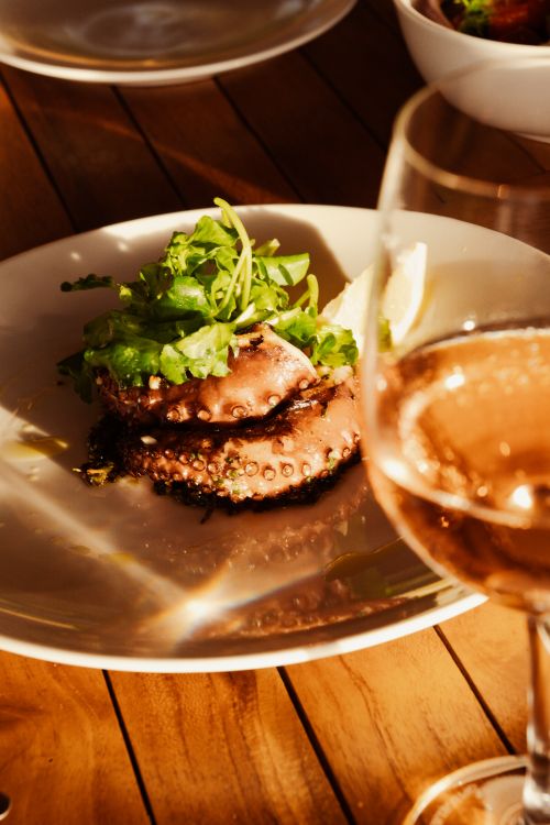 Free Gourmet octopus dish garnished with greens, served with rosé wine. Perfect for culinary themes. Stock Photo