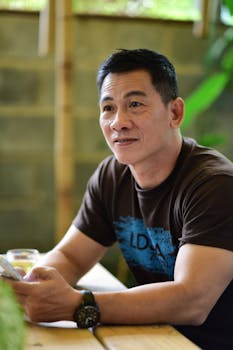 Relaxed man in outdoor café holding smartphone, wearing a watch.